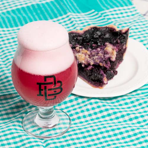 Bright red gose style beer in a glass next to blueberry pie slice