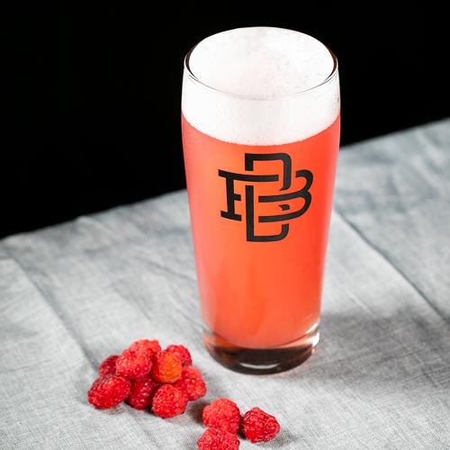 Pinkish tinted beer in a branded glass with whole raspberries