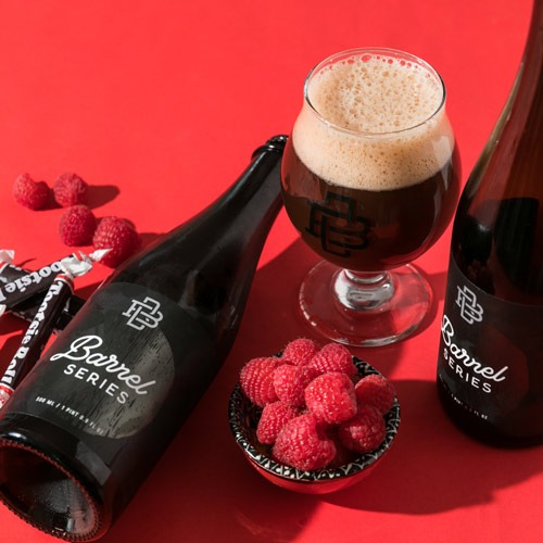 Barrel-Aged bottles with pour of beer and a pile of raspberries